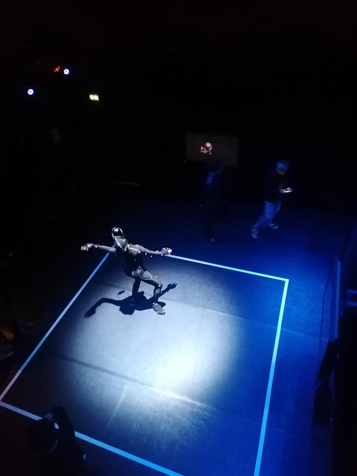Vue plongeante sur une performeuse en combinaison à marqueurs dans un carré de lumière bleue